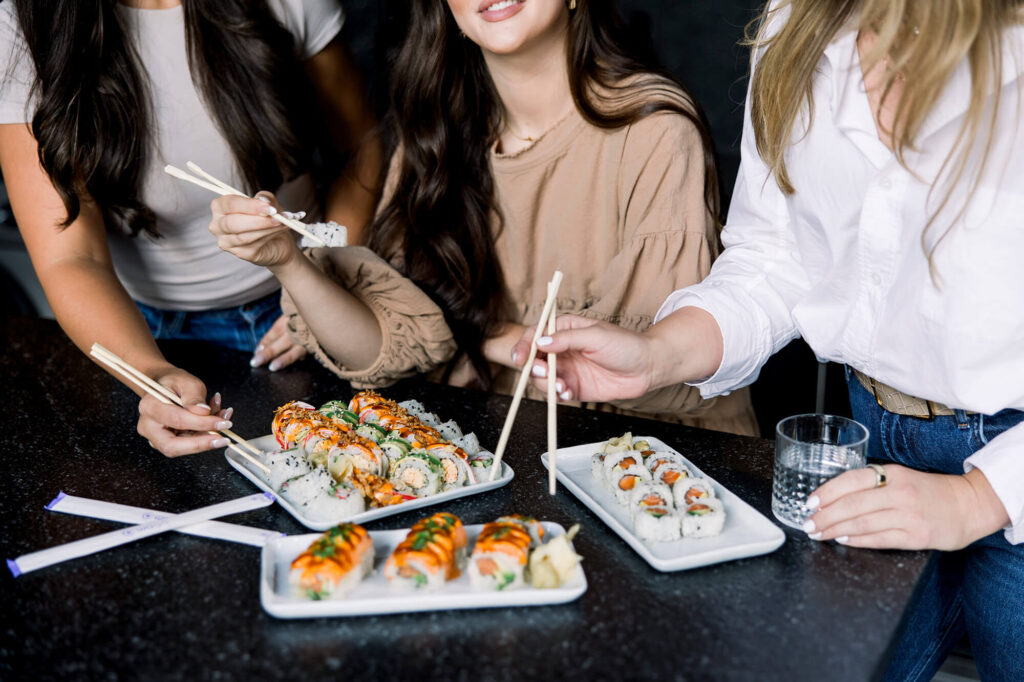 Three women eating 3 plates of sushi with chopsticks